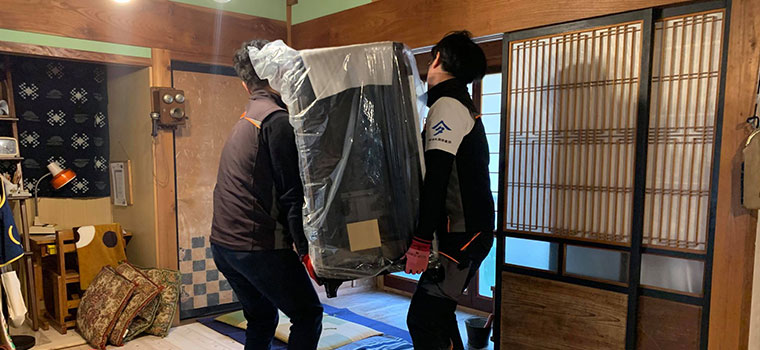 梱包したままのペレットストーブを、二人がかりで古民家の玄関から運び入れているところ