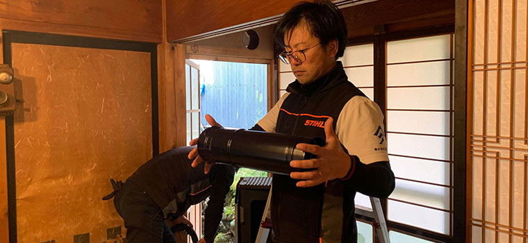 蛇腹状に伸縮する黒い貫通部の煙突を手に取り、長さを確かめている施工担当者