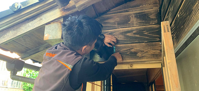 屋外の壁に取り付けた排気口のまわりを、手で押さえて防水処理をしている施工担当者