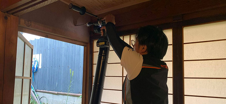脚立に上がり、壁の高い位置に工具をあてて中心の印を付けている施工担当者
