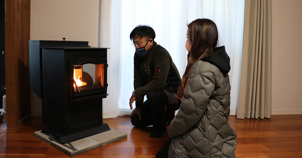 火が入ったペレットストーブの前にしゃがみ、住まい手に使い方を説明する施工担当者